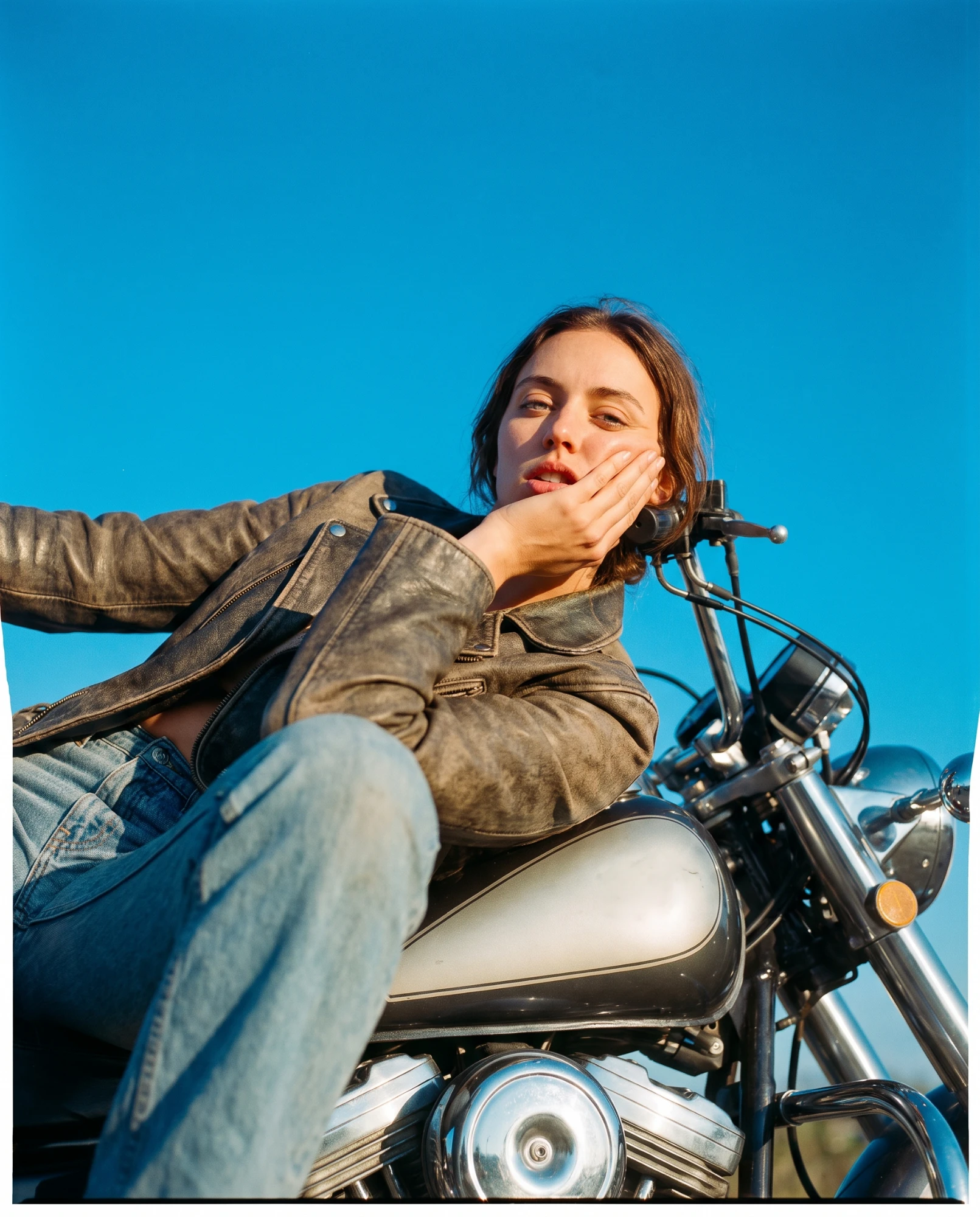 Editorial de moda en contrapicado: cazadora de cuero envejecido sobre una moto clásica bajo cielo despejado