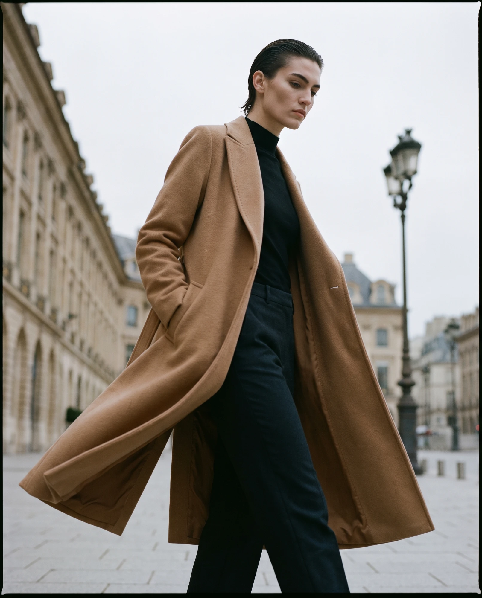 Editorial de moda en calle: abrigo largo de lana camel sobre punto y pantalón negro en una plaza parisina