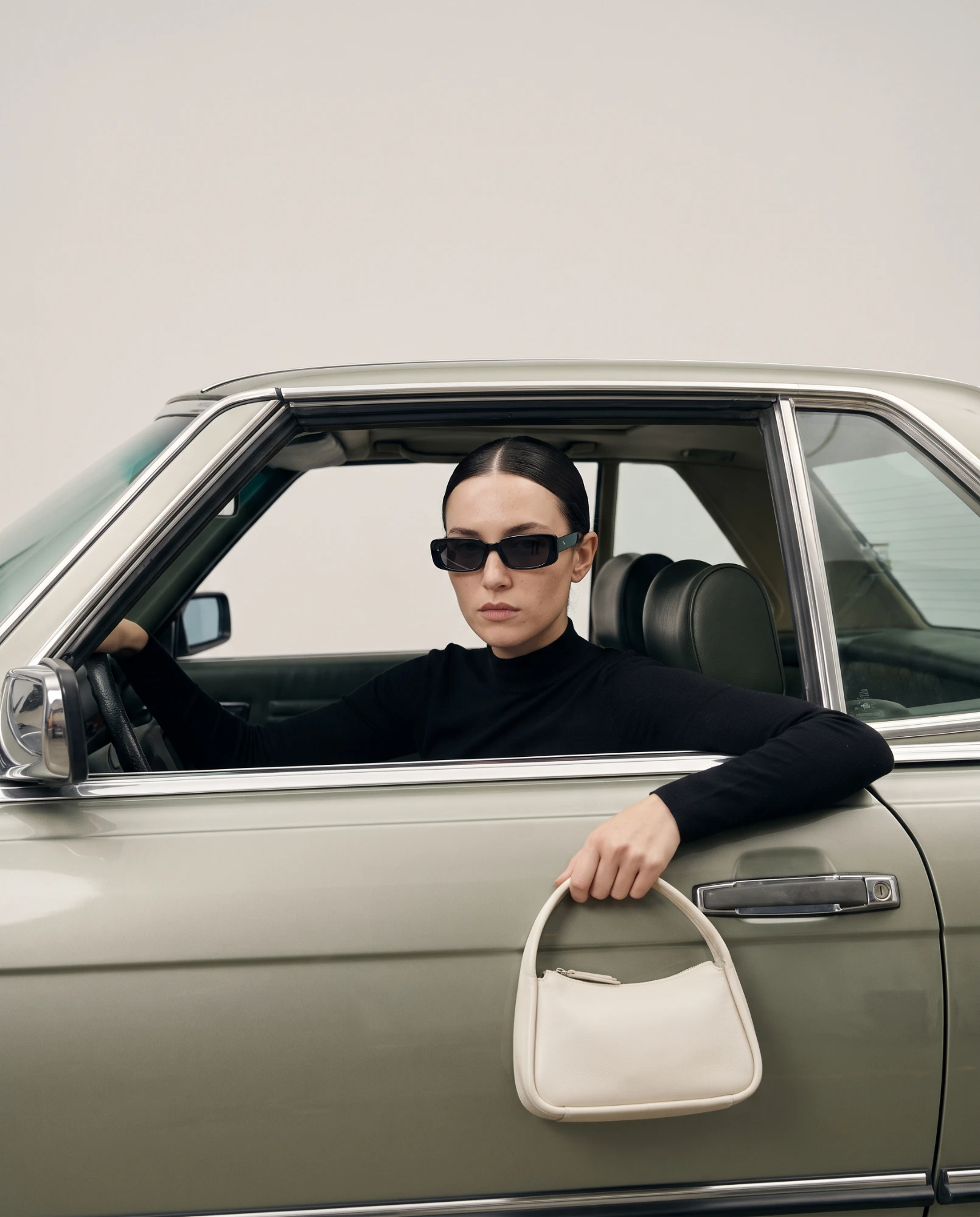 Editorial de moda: punto negro de cuello alto y bolso de piel crudo al volante de un coche clásico